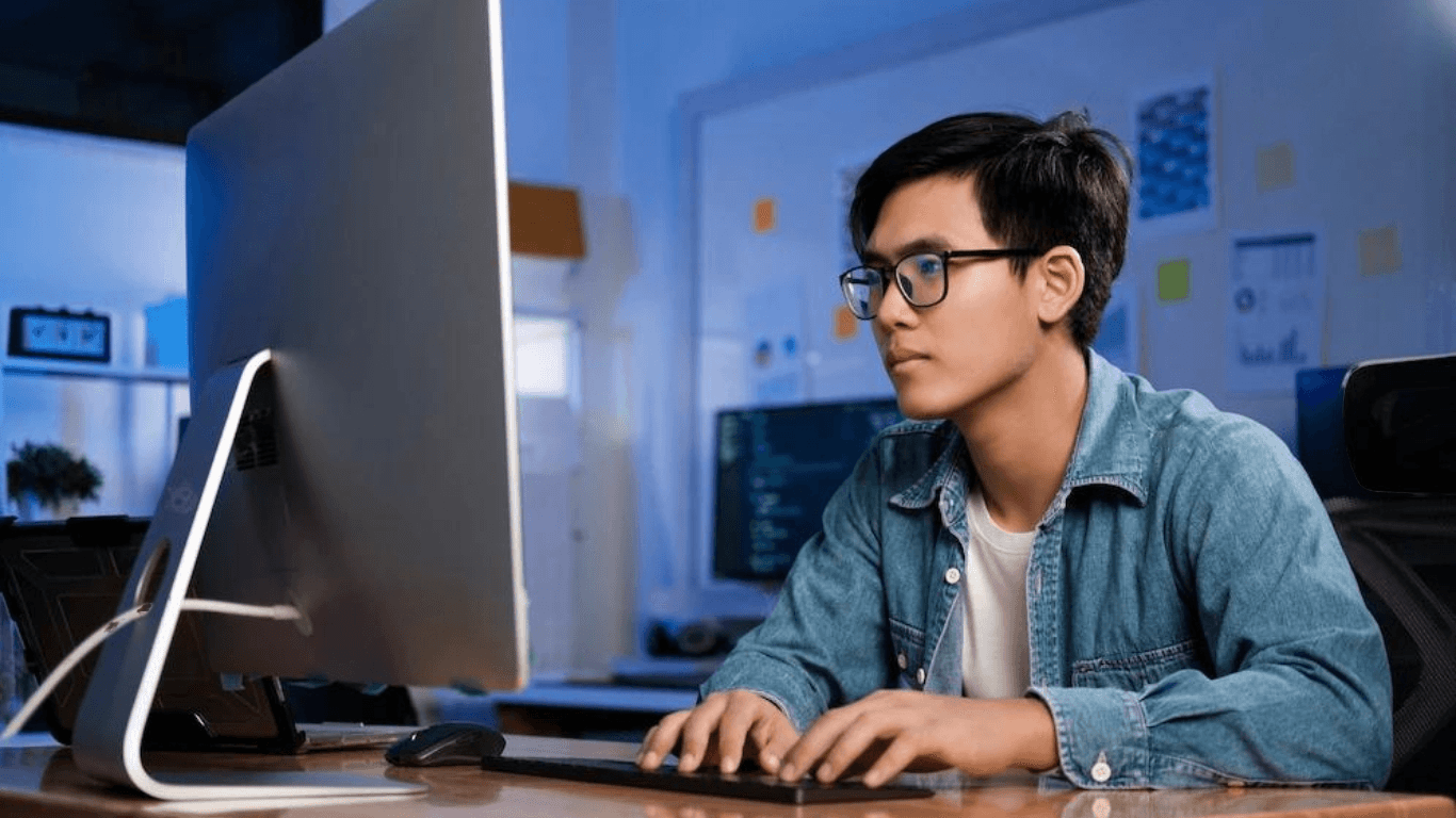 A male graphic designer typing on his keyboard in front of a desktop computer
